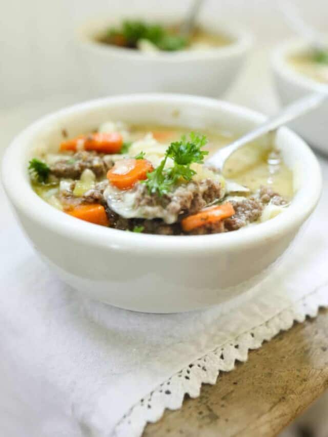 3 bowls of cheeseburger soup in white bowls with spoons on top of a wood table with white table runner.