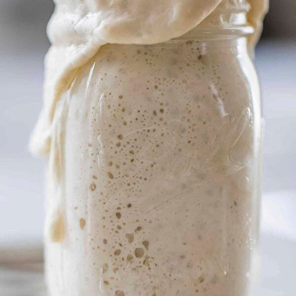 sourdough starter overflowing out of a mason jar on a white countertop.