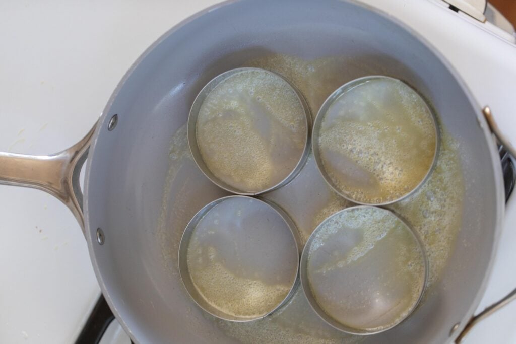 Heating English muffin rings in a skillet with butter.