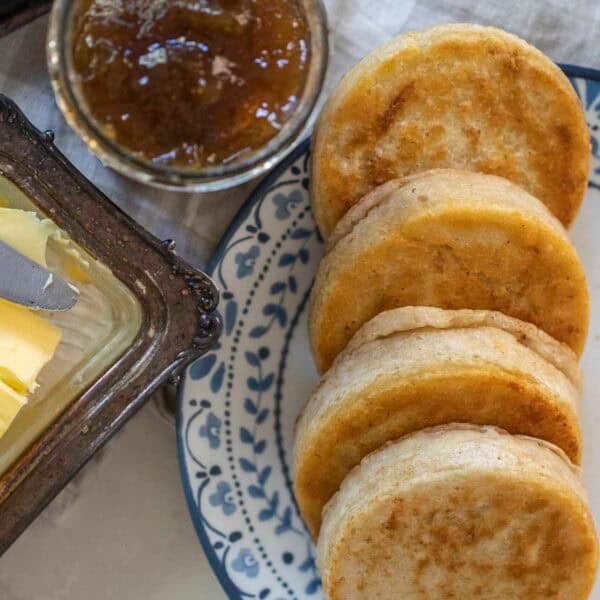 four sourdough crumpets lined up on a blue and white plate with a jar of jam to the left