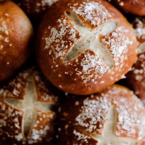 sourdough pretzel buns topped with course salt stacked on a white countertop