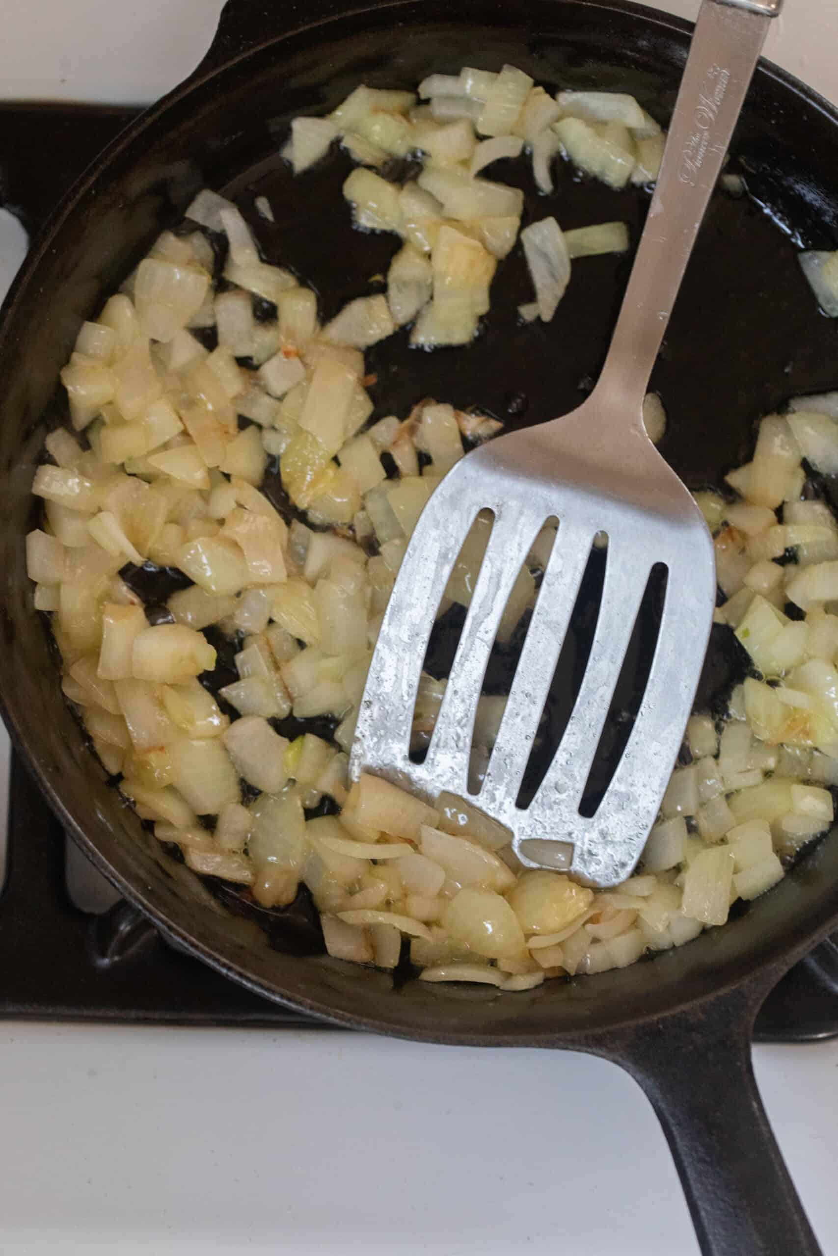 Onions cooking in a cast iron skillet with a metal spatula 