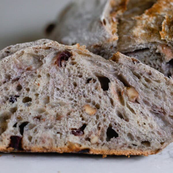 a slice of sourdough cranberry walnut bread propped up on the rest of the loaf on of a white countertop