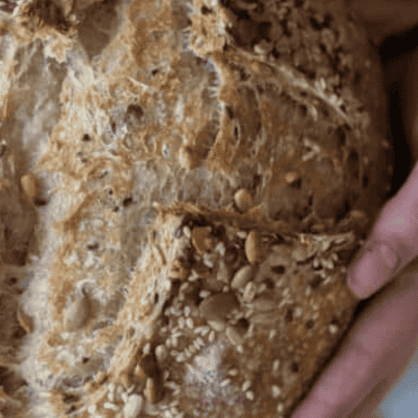 A hand holding a seeded sourdough loaf