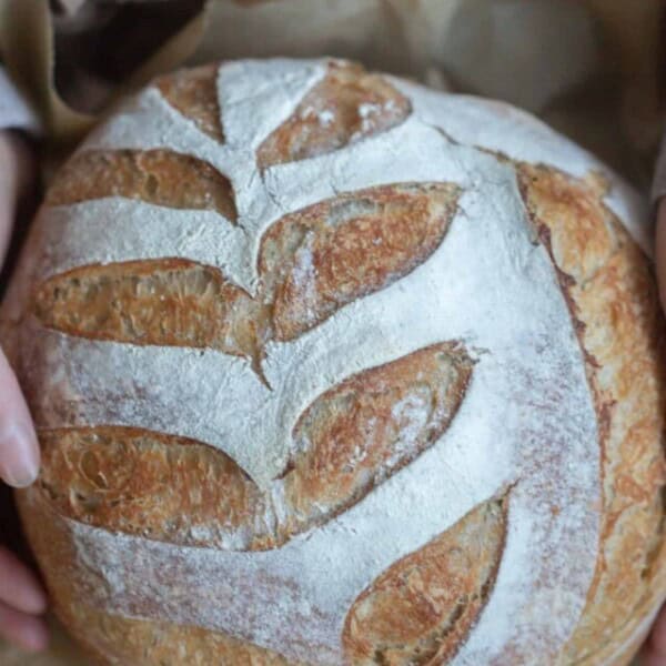 hands holding a loaf of honey sourdough bread on parchment paper