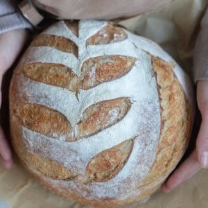 Honey sourdough loaf held in a woman's hands with parchment paper underneath