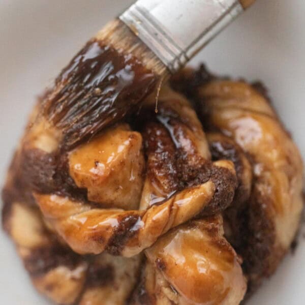 A Swedish cinnamon bun on a white countertop being brushed with a brown sugar glaze