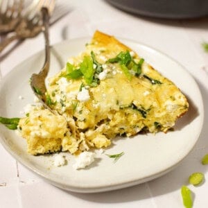 A piece of chicken frittata on a white plate with a fork and a cast iron skillet in the background