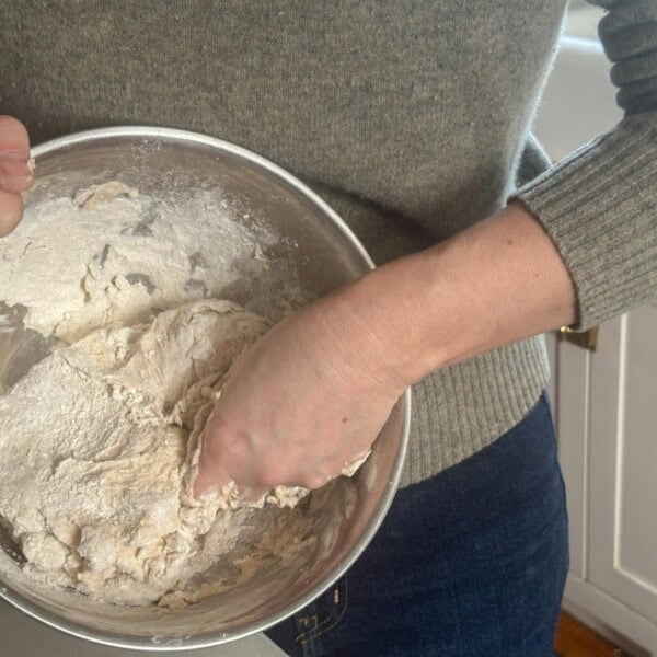 woman mixing sourdough dough by hand in a silver bowl