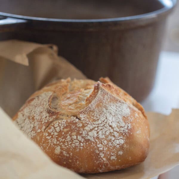 A small batch sourdough loaf on parchment paper with a dutch oven in the background