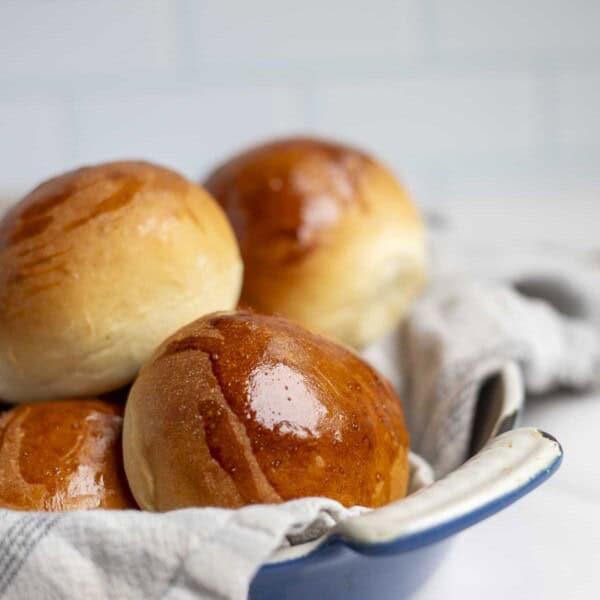 side view of soft fluffy sourdough discard rolls in a blue dish liked with a cream and blue plaid towel