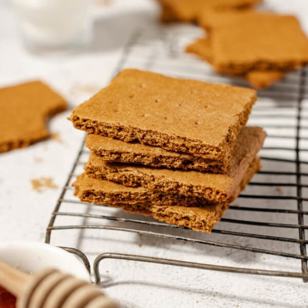 stack of homemade sourdough graham crackers on a wire rack surrounded by honey, milk, and more crackers