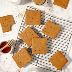 overhead photo of graham crackers spread allover a countertop and wire cooling rack with glasses of milk and honey surrounding the crackers