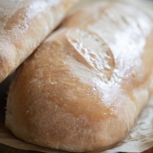 two loaves of sourdough Italian bread stacked on each other on parchment paper