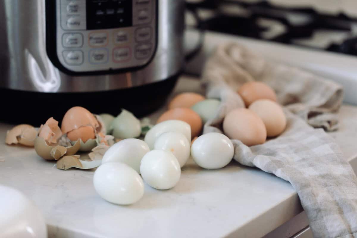 Peeled hard boiled eggs in front of a Instant Pot on a white countertop.