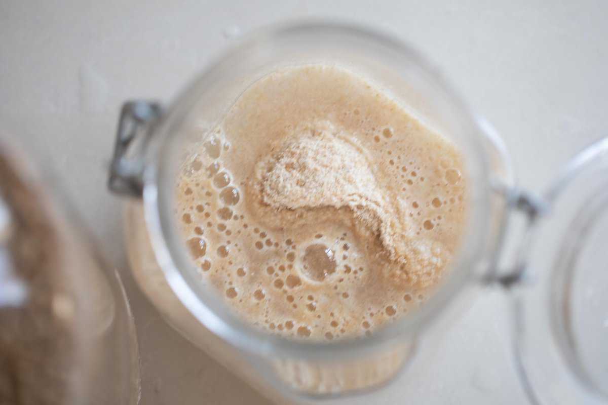 water and whole wheat flour in a jar on a white countertop.