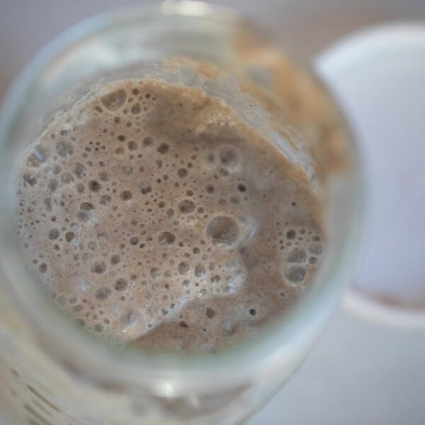 bubbly rye sourdough starter in a glass jar with a white plastic lid to the left