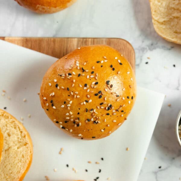 overhead photo of sourdough hamburger buns made with discard on a marble countertop, a cutting board with a plate on top