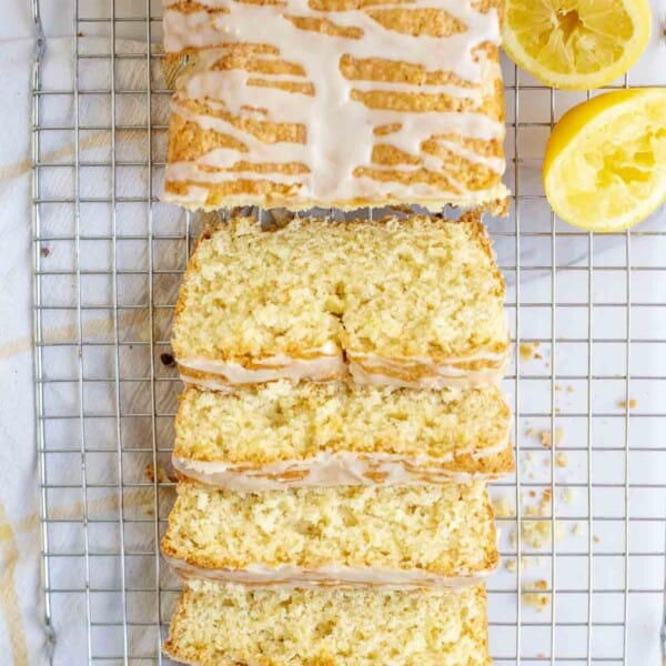 overhead photo of sourdough lemon discard bread loaf topped with icing on a wire rack. Half of the loaf sliced. lemons surround the bread