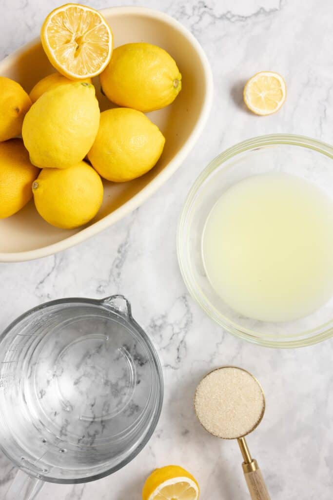 lemons in a bowl, jars of whet water and a scoop of sugar on a countertop