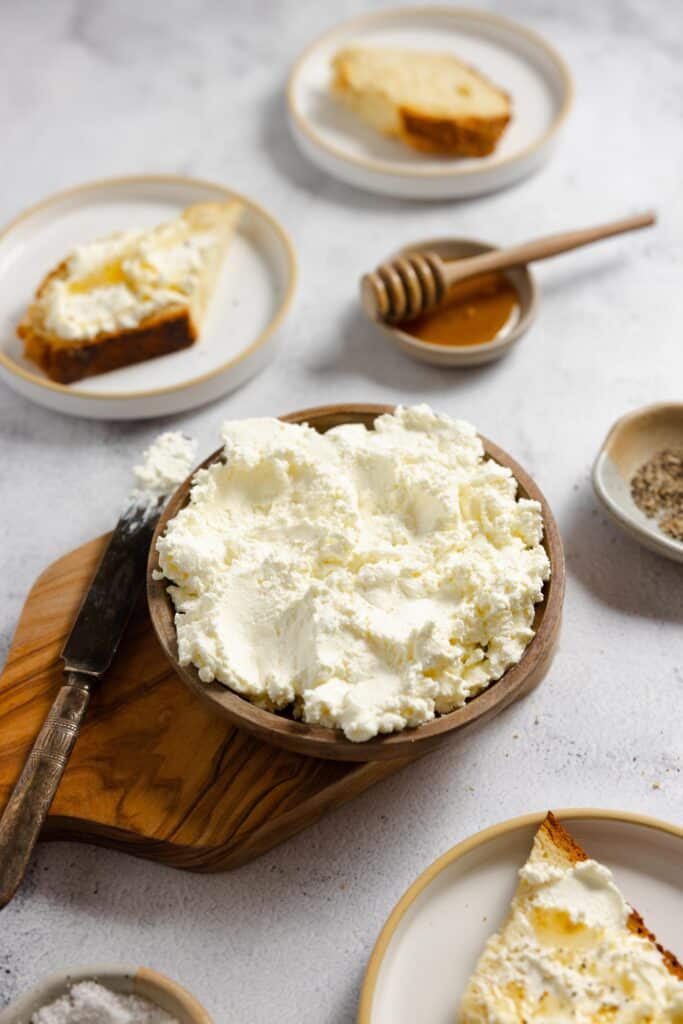 a wooden bowl of ricotta with white plates of ingredients surrounding the bowl
