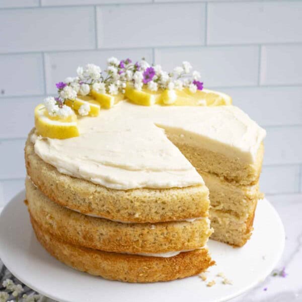 Sourdough lemon cake with a slice missing on a white cake platter with a white tile background