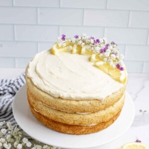 Layered sourdough lemon cake with white icing and lemon slices and edible flowers as decorations on a white cake platter