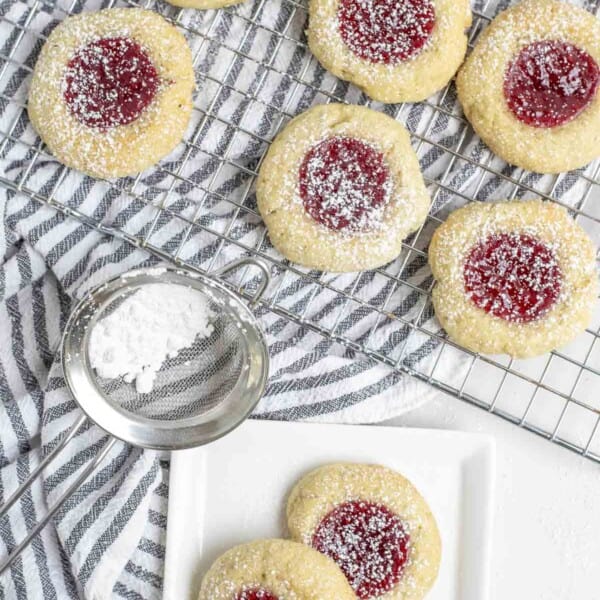 two thumbprint sourdough cookies on a white plate. More cooking on a cooling wrack on top of a white and black stripped towel in the background.