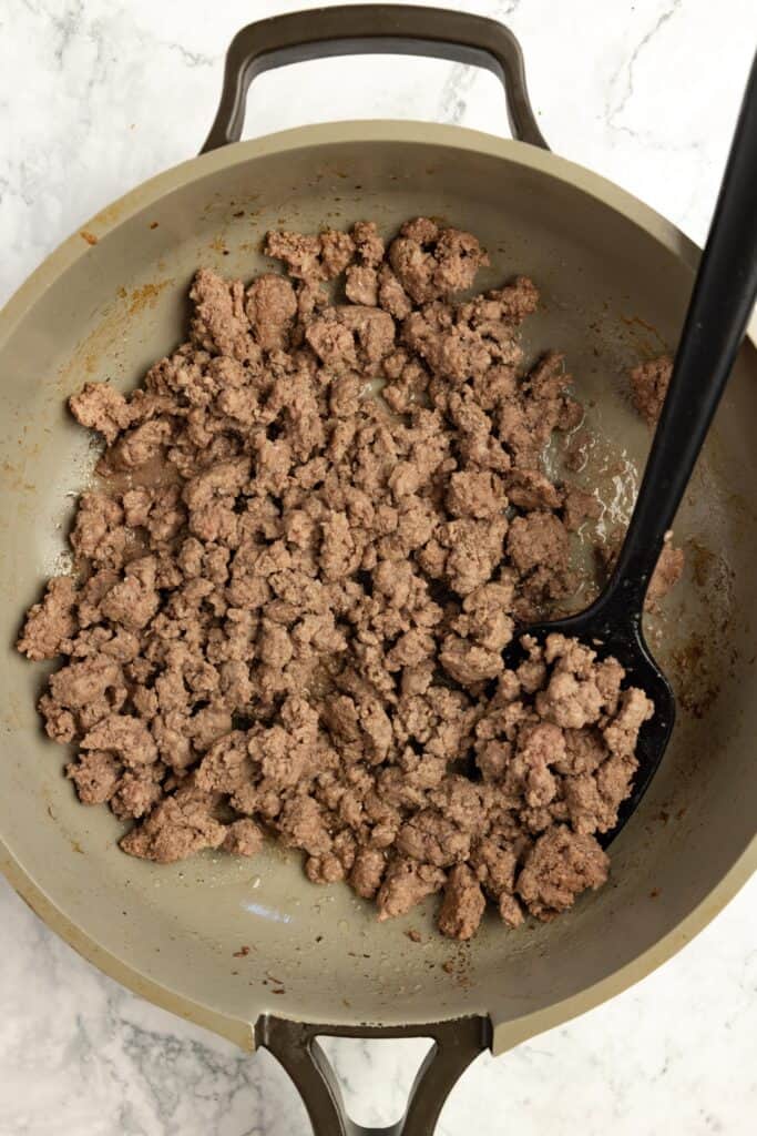 Ground beef browned in a skillet with a black spoon.
