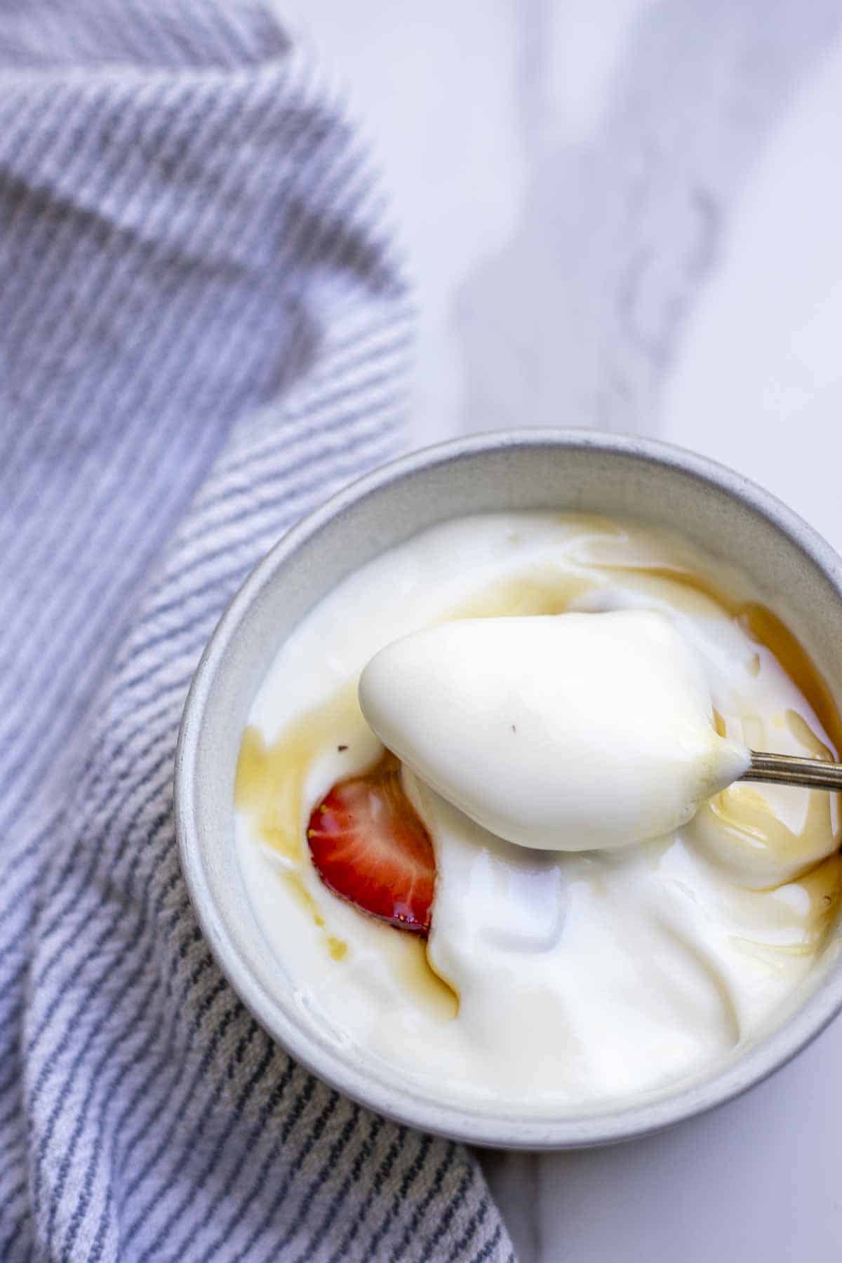 spoonful of yogurt over a bowl of yogurt with maple syrup and strawberries