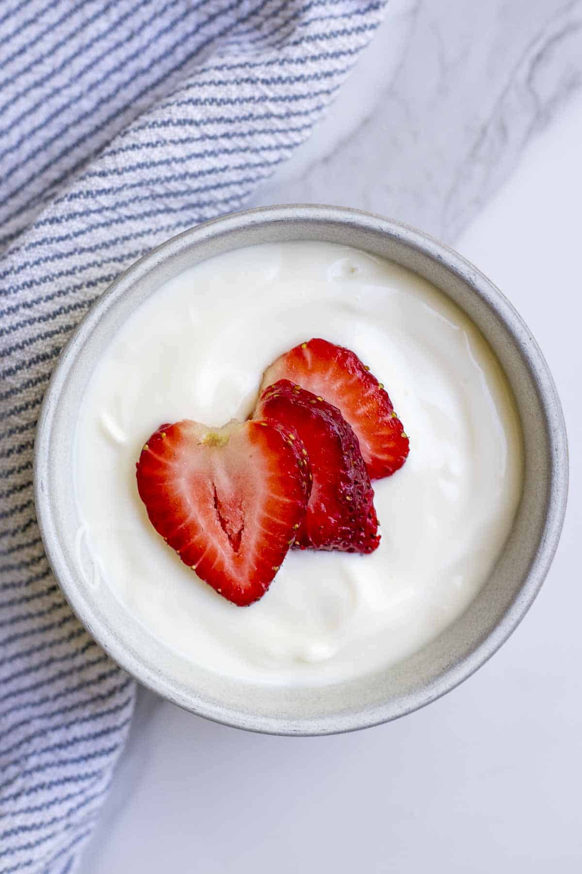 sliced strawberries on top of raw milk yogurt in a bowl