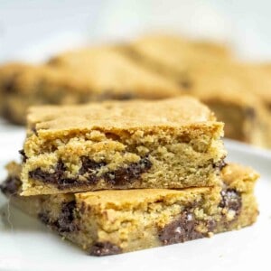 two slices sourdough blondies on a white plate with more blondies in the background