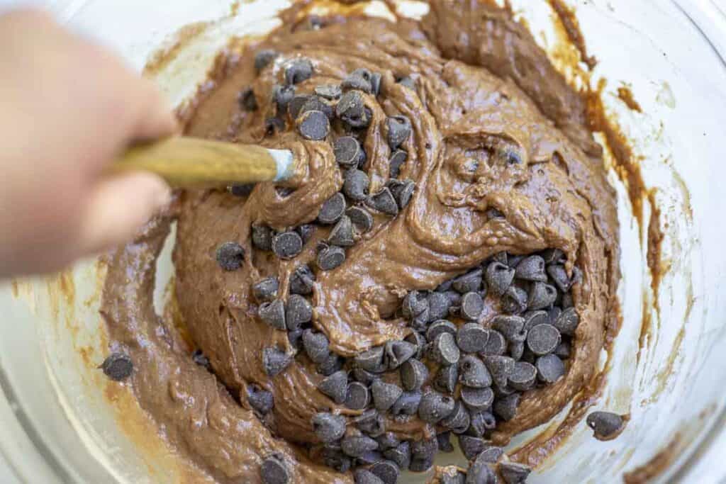 Stirring chocolate chips into chocolate bread batter in a glass bowl