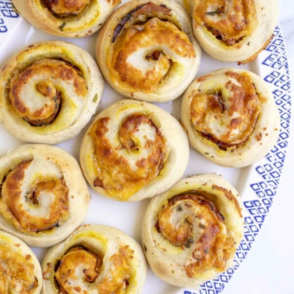 Sourdough ham and cheese rolls on a white platter with blue decorative edge on a white countertop