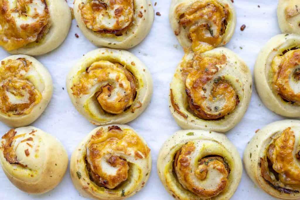 12 freshly baked ham and cheese rolls on a parchment paper lined baking sheet
