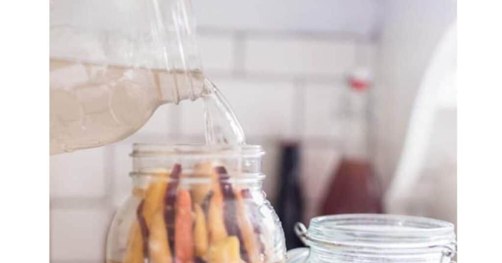 A mason jar full of water pouring into a mason jar filled with carrot sticks.