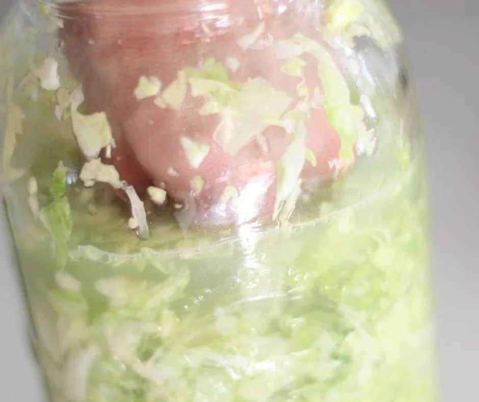 A wooden fermentation tool smashing down the cabbage in a mason jar so everything is underneath the brine. 