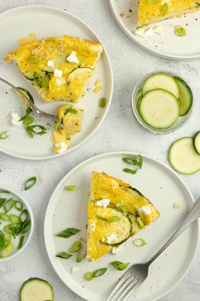Slices of zucchini frittata on white plates with forks.