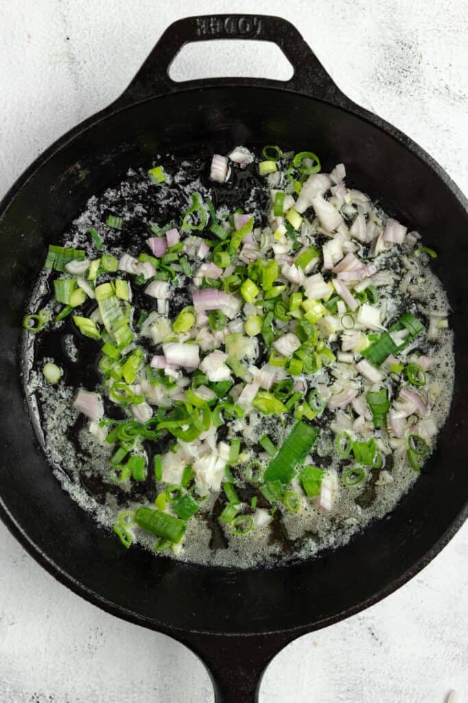 shallot, greek onions and zucchini sautéing in a cast iron skillet.