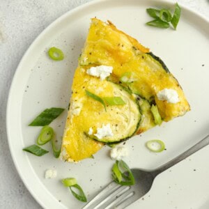 Slice of zucchini frittata topped with herbs on a white plate.