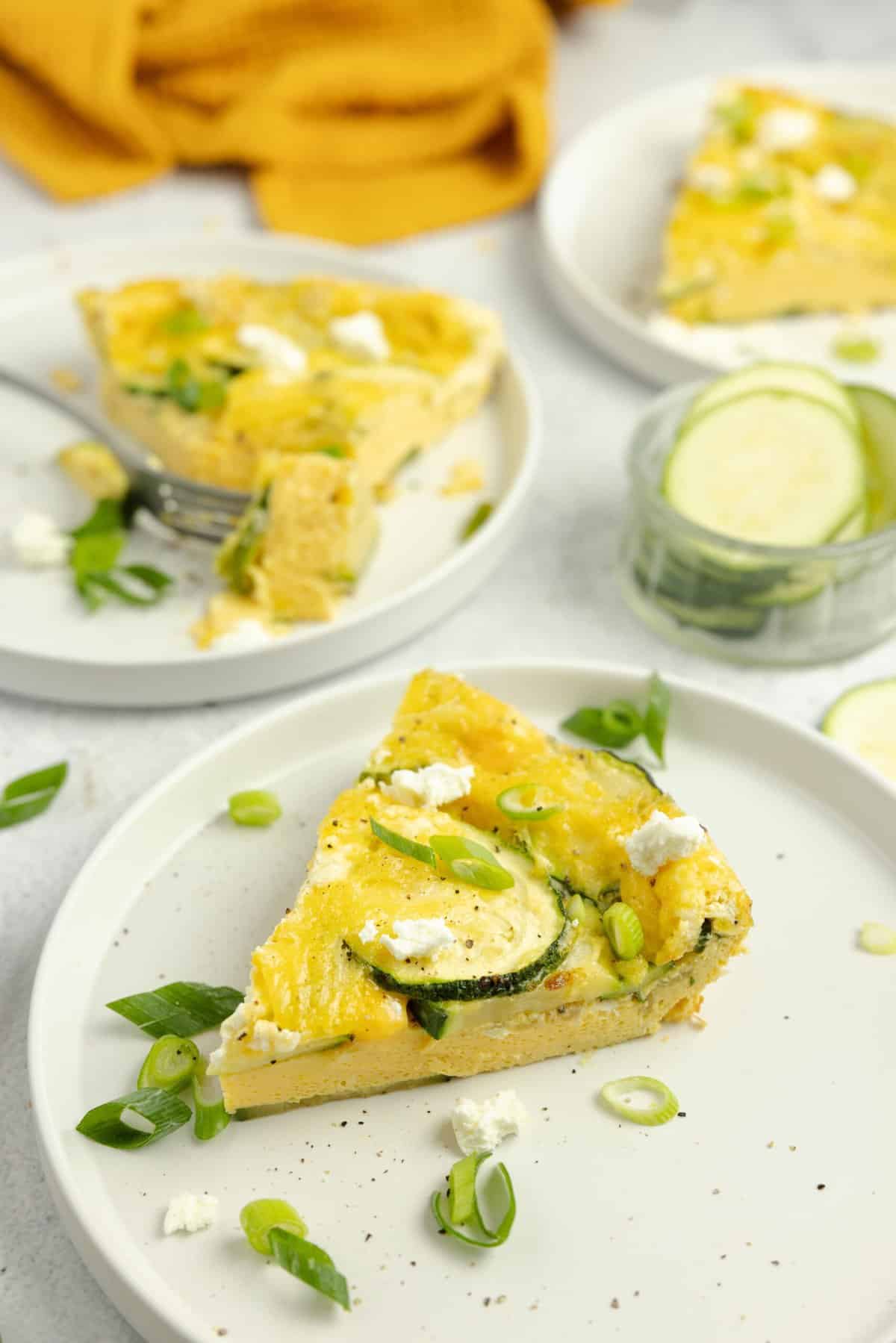 slices of zucchini frittata on white plates topped with fresh herbs.