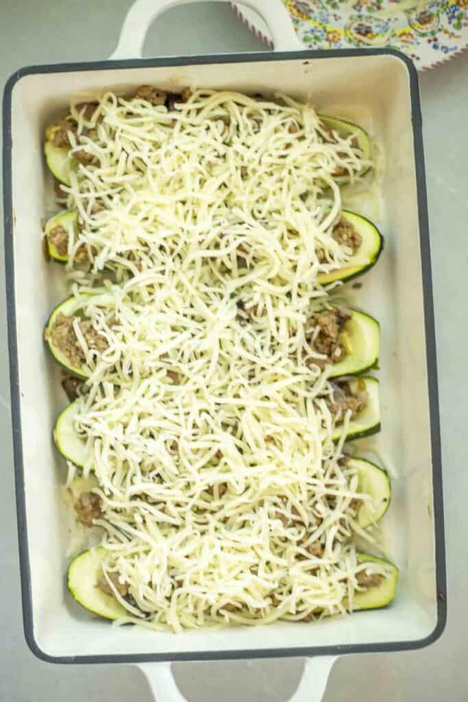 cheese topped on sausage stuffed zucchini boats in a baking dish.
