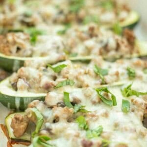 Sausage stuffed zucchini boats topped with cheese and fresh herbs in a white baking dish.