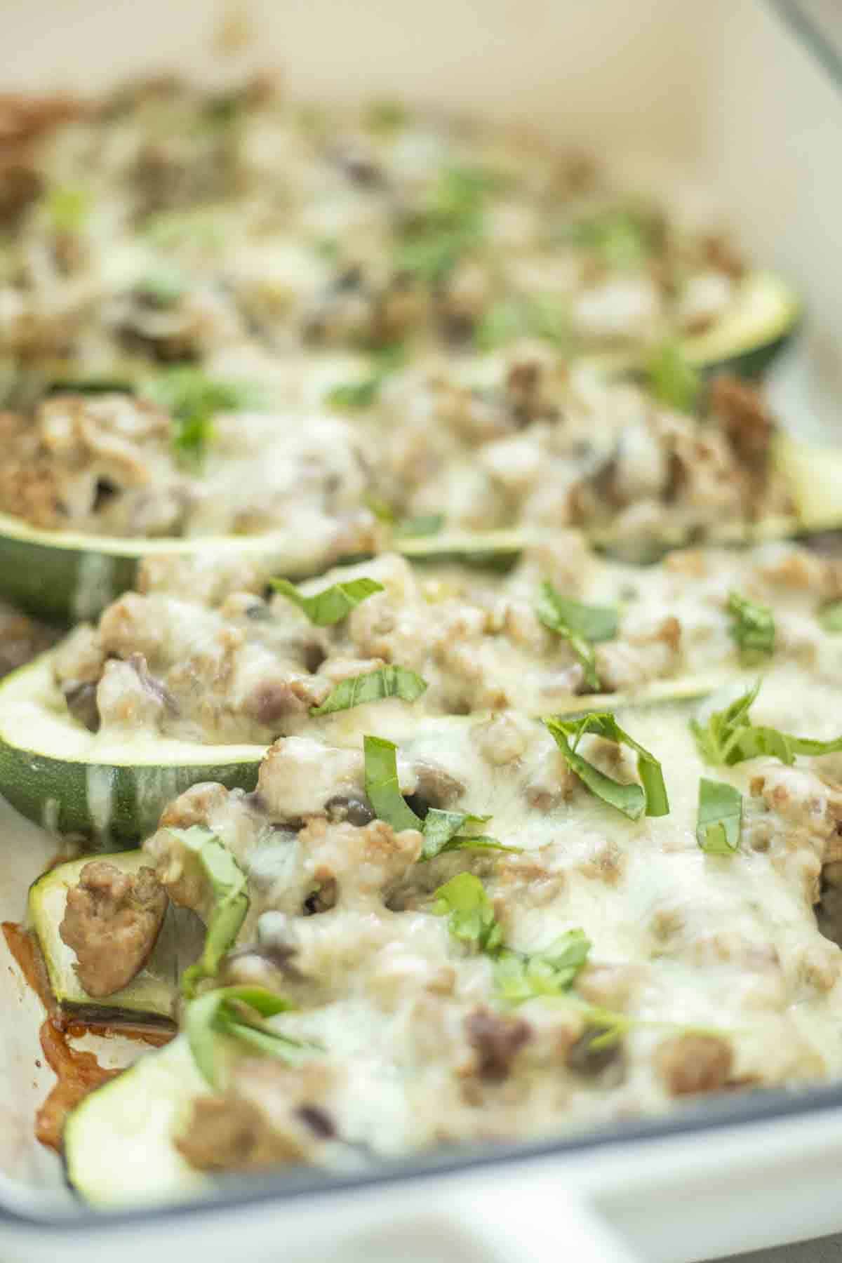 Sausage stuffed zucchini boats topped with cheese and fresh herbs in a white baking dish.
