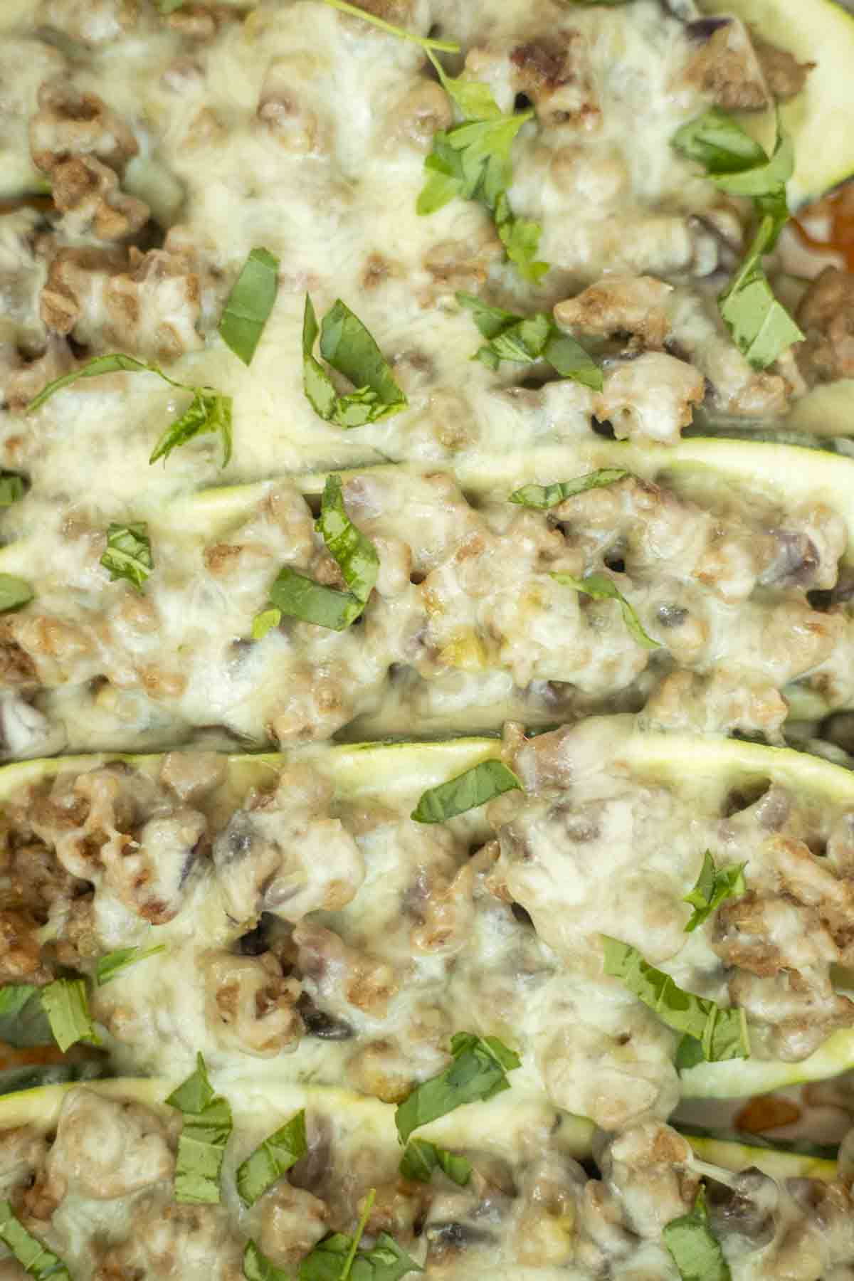close up picture of sausage zucchini boats topped with cheese and herbs.