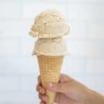 A hand holding a waffle cone topped with two scoops of date ice cream.