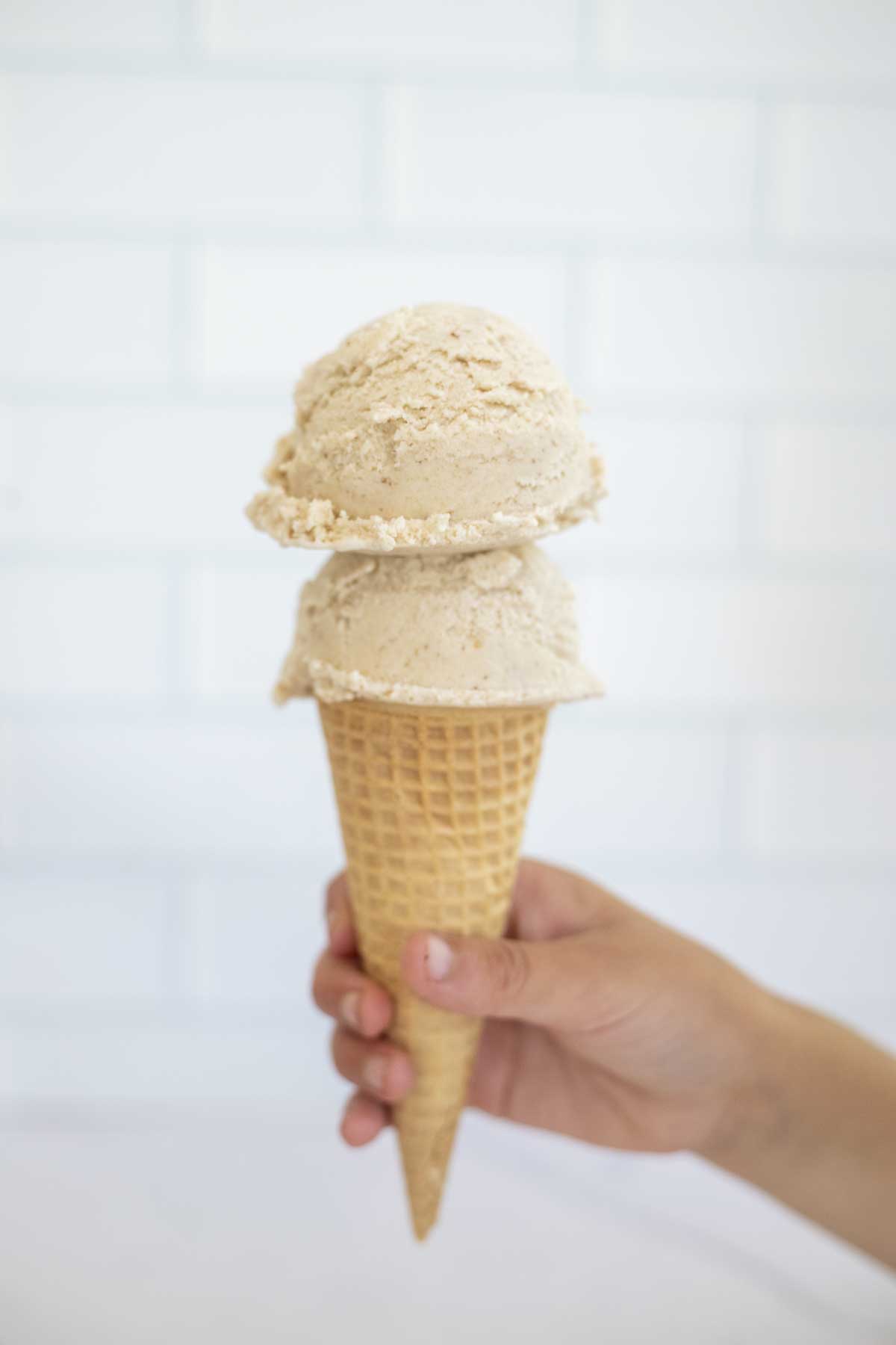 A hand holding a waffle cone topped with two scoops of date ice cream.