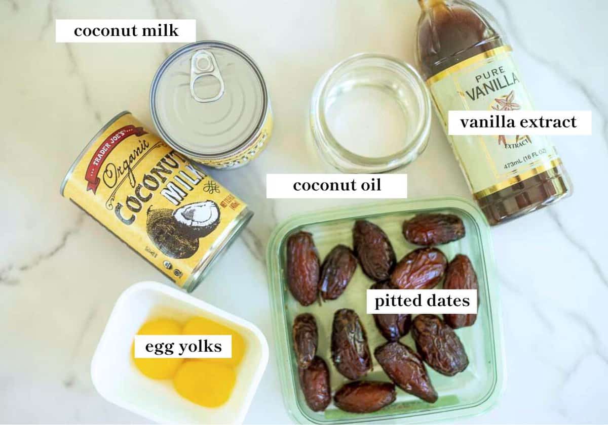 Dates, egg yolks, a can of coconut milk, coconut oil, and vanilla extract on the counter.