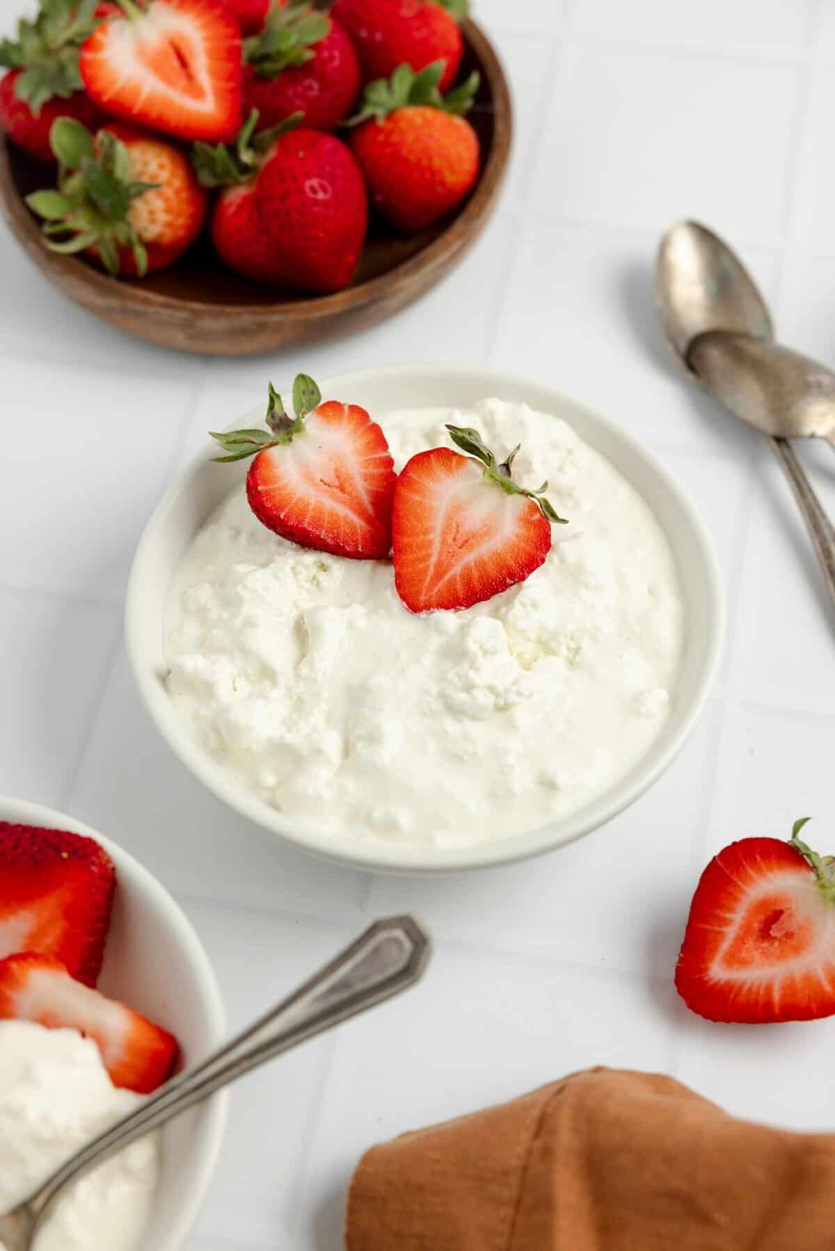 cottage cheese in a bowl with strawberries, more strawberries surround the bowl.