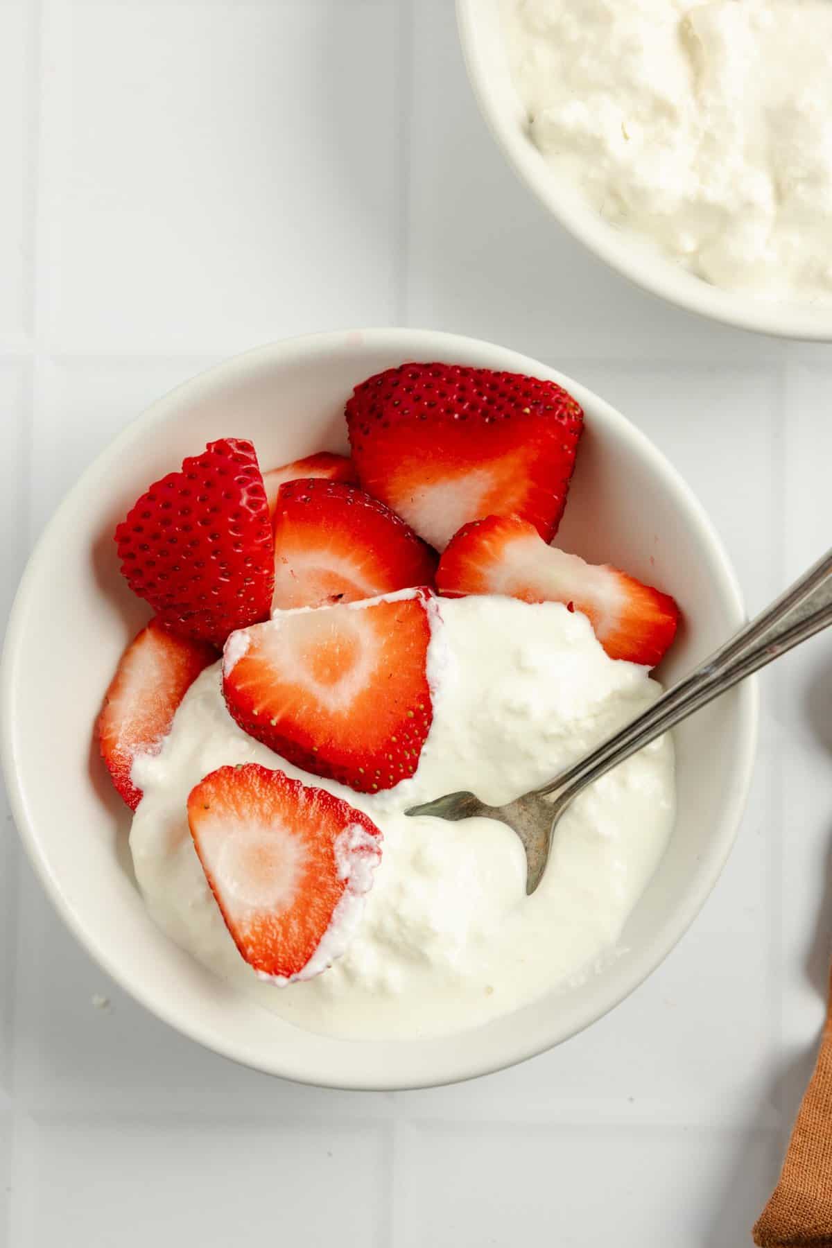 spoonful of cottage cheese coming out of a bowl with strawberries.